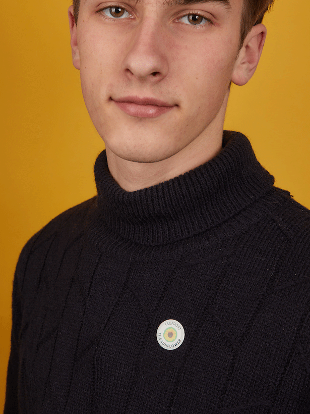 Young man wearing a dark blue jumper and a circular white pin badge with Sunflower and text ' I support the Sunflower'