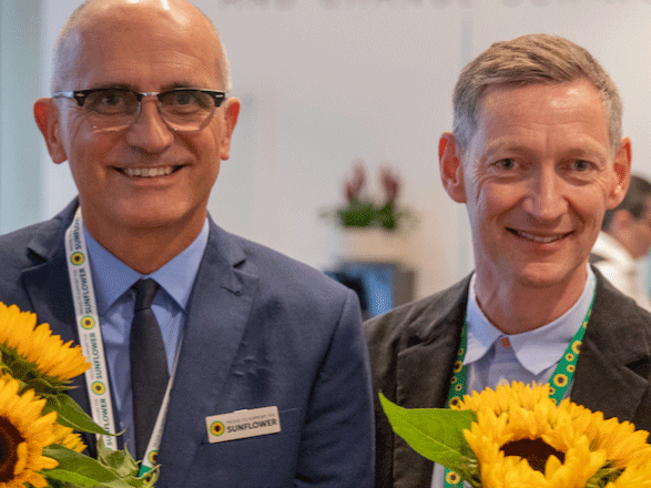 Two men smiling next to bunches of Sunflowers