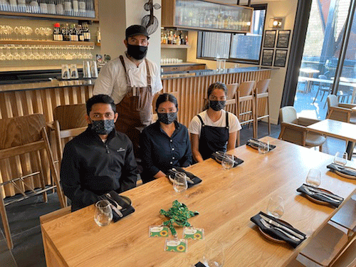Cuatro empleados del hotel con mascarillas se sentaron en una mesa con un miembro más del personal detrás de ellos.