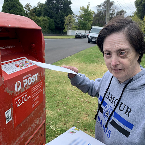 Image of woman posting letters in a red letterbox width=