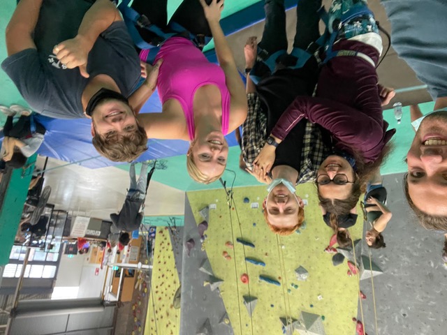 Five people smiling standing in front of climbing wall