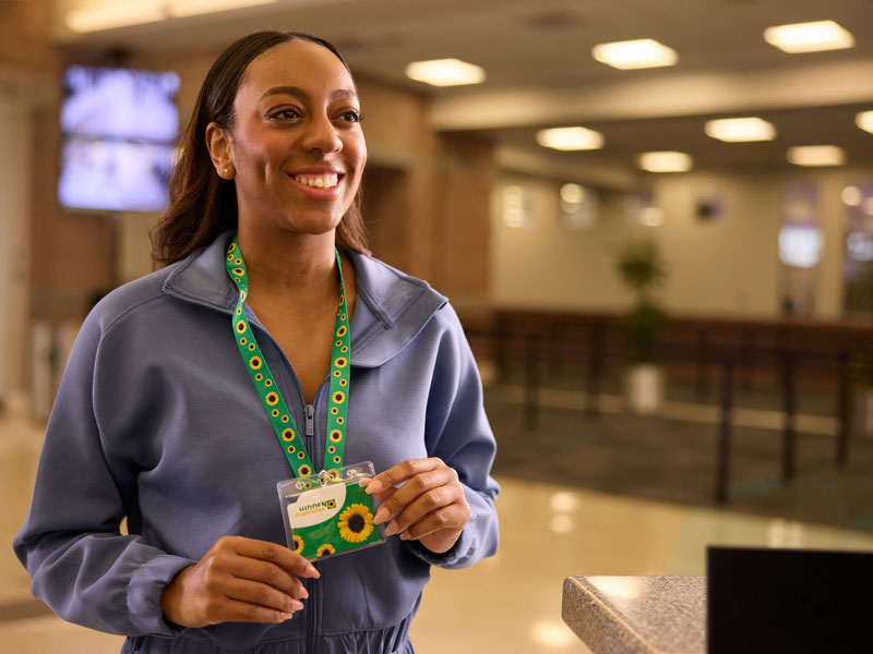 A woman smiling wearing a blue shirt and a green Sunflower lanyard and ID card