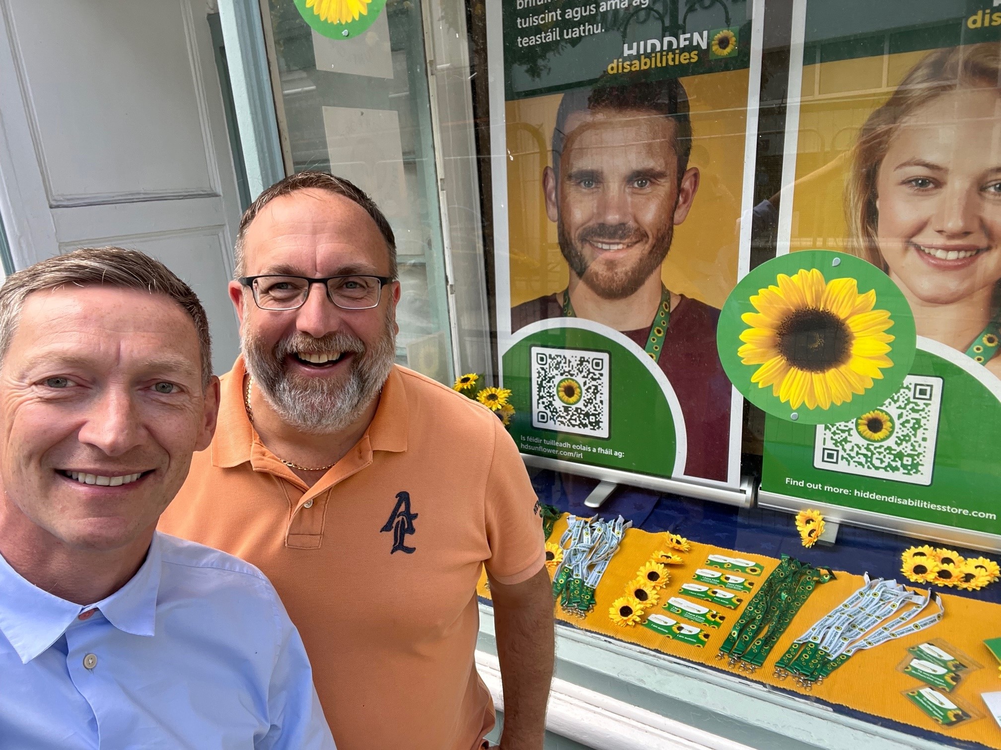 Paul and Tristan from Hidden Disabilities Sunflower stand outside the pop up shop in Ennis. A vibrant window display is visible. Showcasing Sunflower products