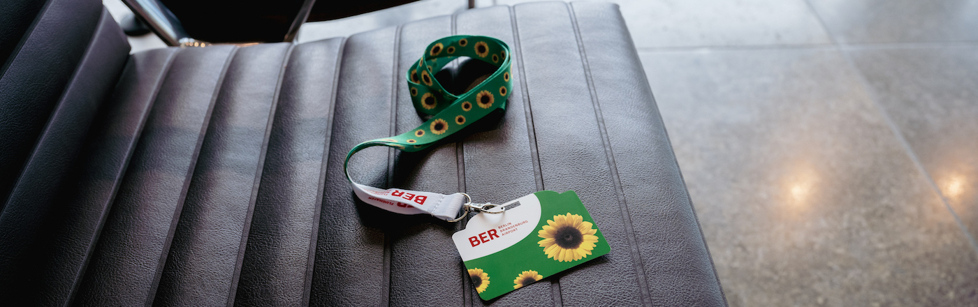 A black seat in an airport passenger terminal. On the seat is a Sunflower lanyard and card with the BER airport logo on 