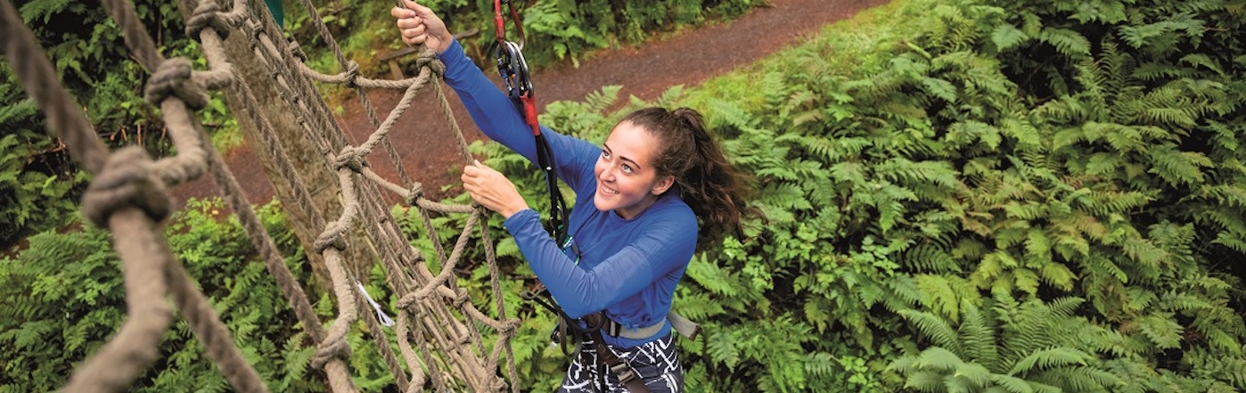 A young woman climbs up a rig of netting above a forest canaopy