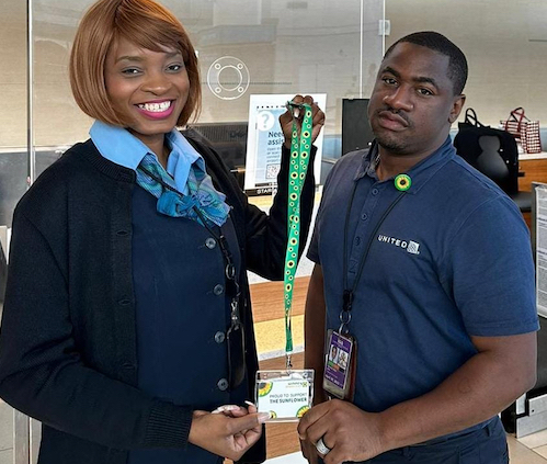 A black woman and black man wearing navy blue on  their training day. She holds a sunflower lanyard. He wears a sunflower pin