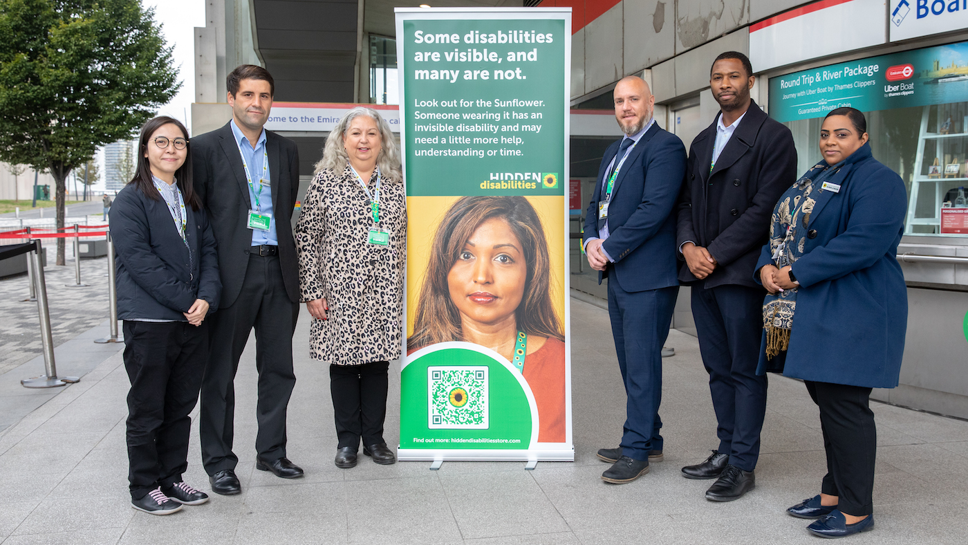 Um grupo de pessoas fica em frente a um banner do Hidden Disabilities Sunflower 