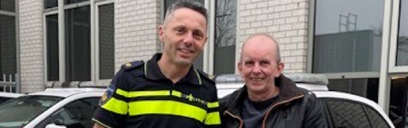 A white policeman stands outside a police station next to Kees from Hidden Disabilities Sunflower. They smile for the camera 