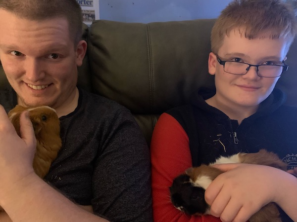 Conor and Rory sit side by side holding their guinea pigs