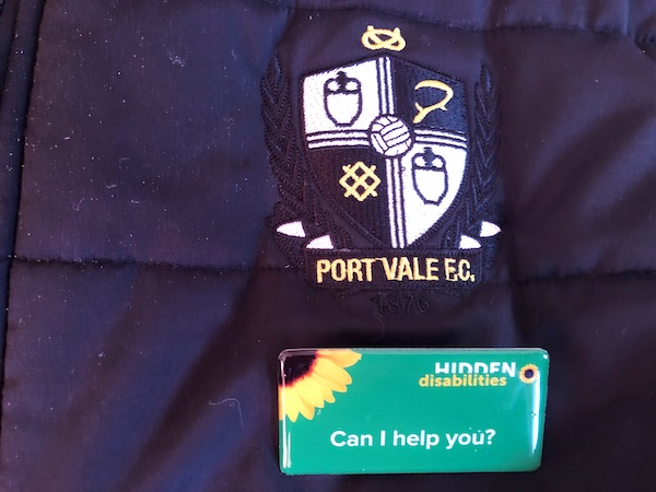 A Portvale security jacket with a hidden disabilities Sunflower badge on that reads: Can I help you?