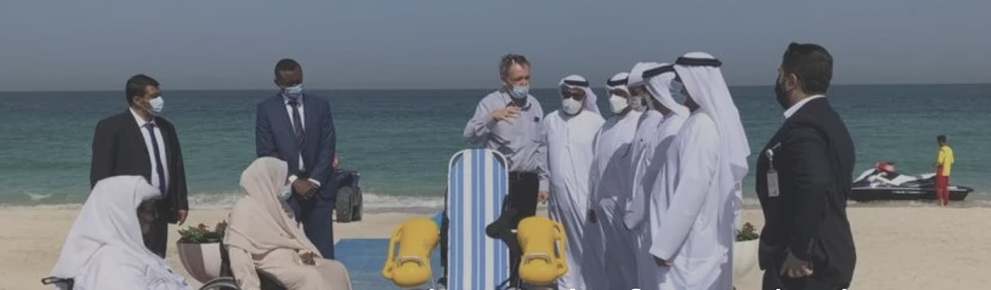 A group of Emiratis on a beach watching Andy from Topland demonstrate a floating wheelchair 