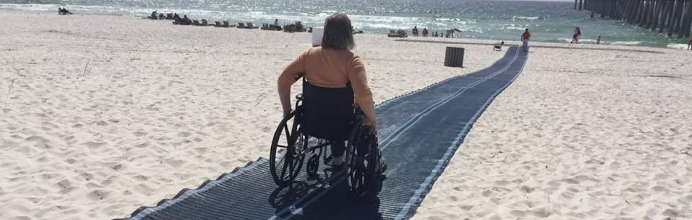 A person in a wheelchair on a beach on a ramp heading to the sea 