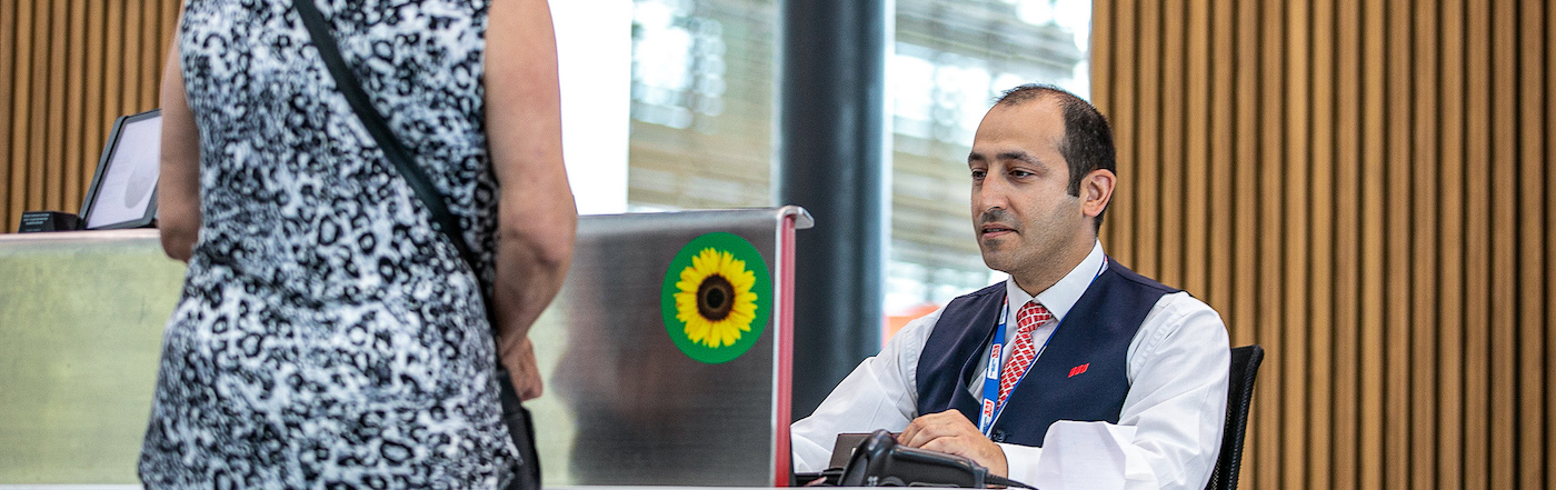 A male employee sits behind the Turkish airlines check in desk. There is a Sunflower sticker displayed. 
